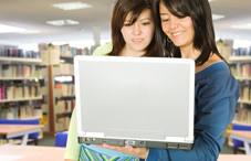 Two young women looking at a laptop in a library 