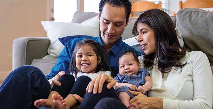 Young latino parents with two small children on their laps