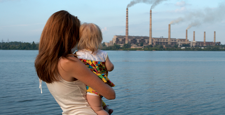 Woman holding a child looking at factory smoke stacks in the distance