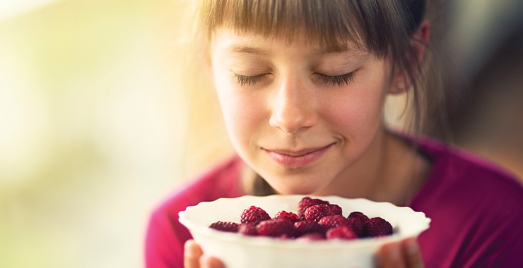 Young girl enjoying the small of clean fresh raspberries 