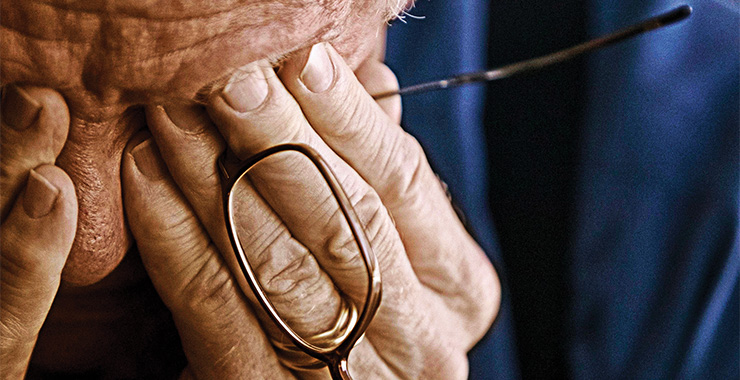 Elderly man with hands over his face