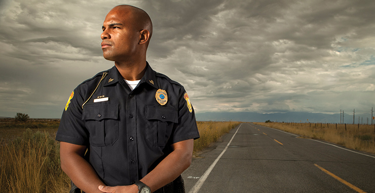 Police officer standing strong in the foreground with a paved road in the background