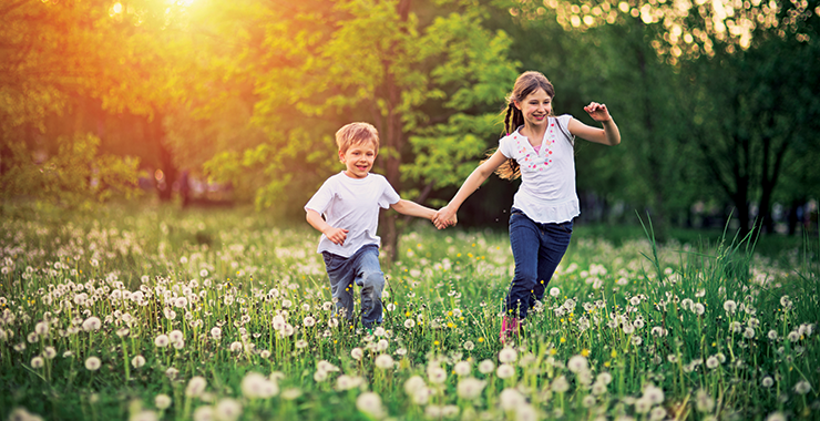Older sister running through a field with younger sibling