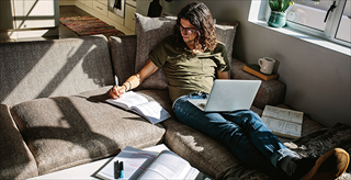man on his couch surrounded by open books and his laptop