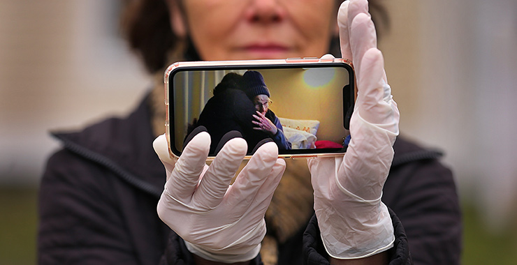 woman with medical gloves holding a phone showing an older woman getting a hug