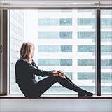 woman sitting on a windowsill looking out at a tall building