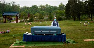man in a non medical mask standing next to a coffin