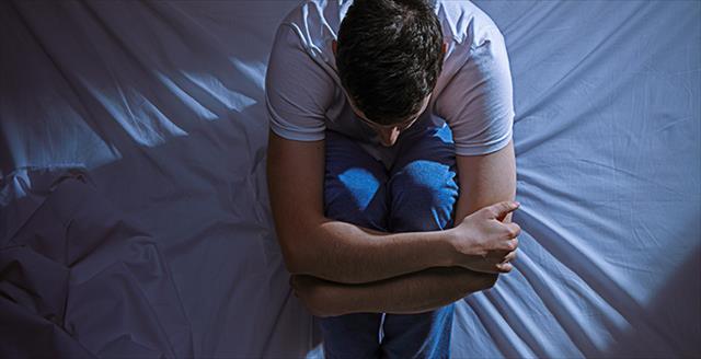 man in pajamas sitting on a bed hugging his knees
