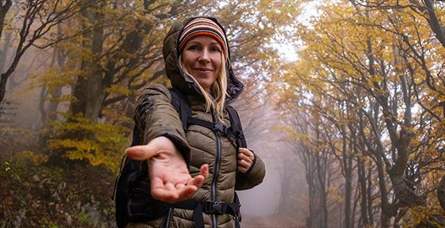 woman walking outside and extending a welcoming arm toward the front of the picture
