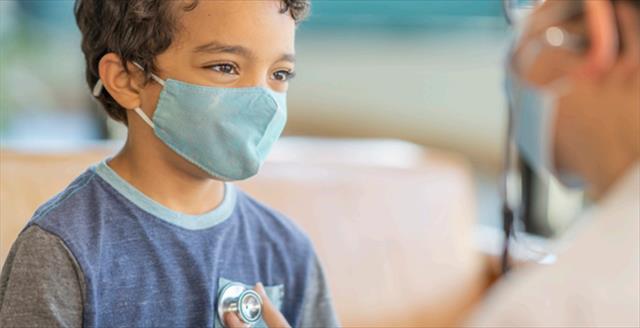 medical professional with a stethoscope listing to the heart of a young boy