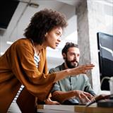 woman explaining something to a man sitting at a computer