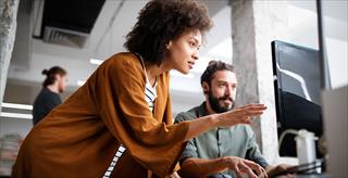 woman explaining something to a man sitting at a computer