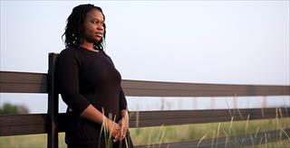 woman of color leaning against a wood fence