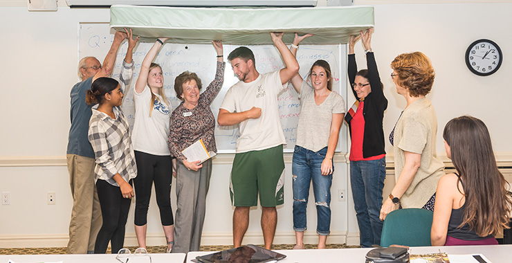 people of various ages holding a mattress in the air