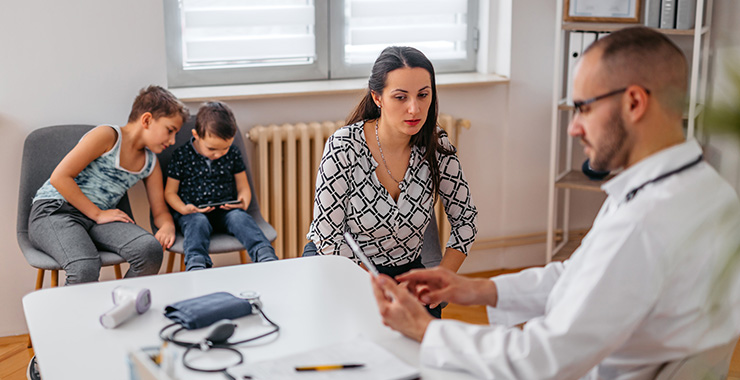 doctor on a video chat while talking to a parent with children sitting in the background