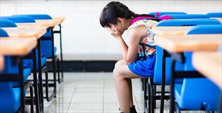 child sitting in a classroom with her head in her hands