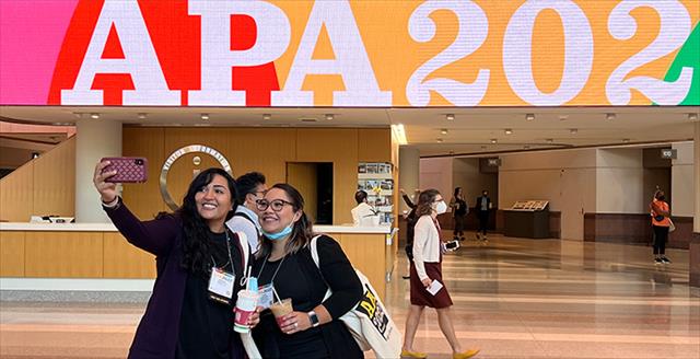 two women taking a selfie in front of an APA 2022 sign