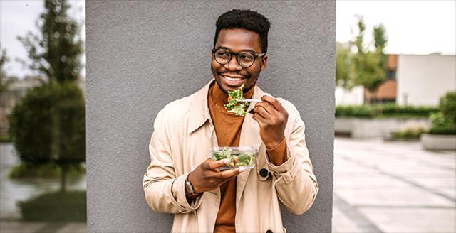 man standing outside eating a salad