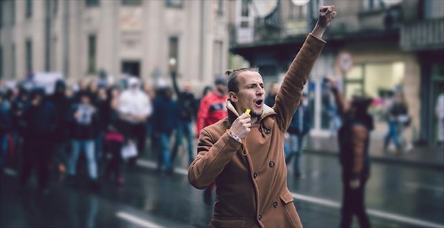 man in a protest march holding a whistle in one hand with his other hand raised with closed fist