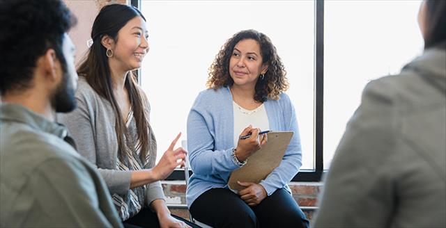 woman holding a clipboard and talking to two young adults