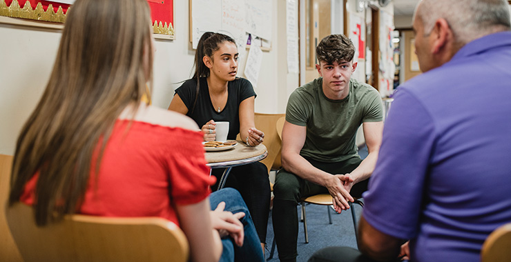 group of students sitting at desks talking with an adult