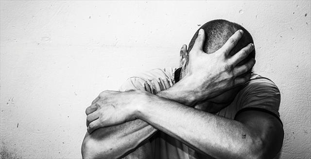 man with arms crossed, head down and hand on head