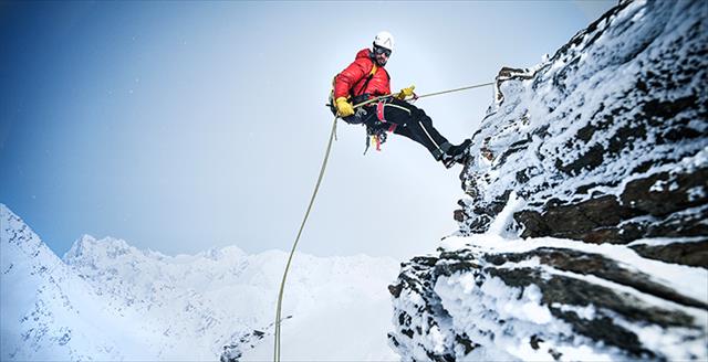 man rappelling down a mountain during the winter