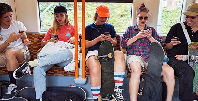 teens with skateboards looking at smartphones