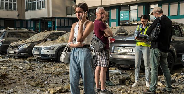 woman talking on a cell phone while standing in the midst of bombed cars and building