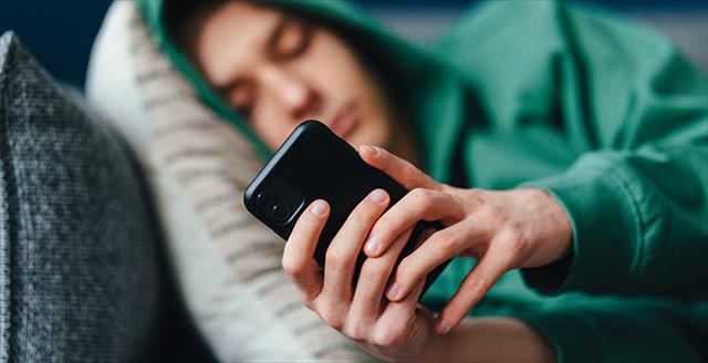 person wearing a hoodie laying down and using a smartphone