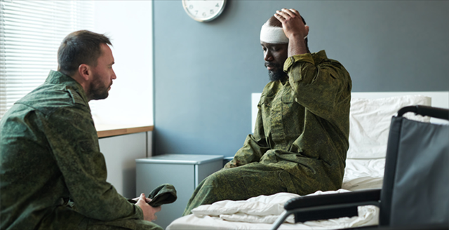 soldier talking with another soldier who is sitting on a hospital bed