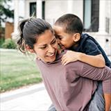 woman smiling, carrying a young child on her back