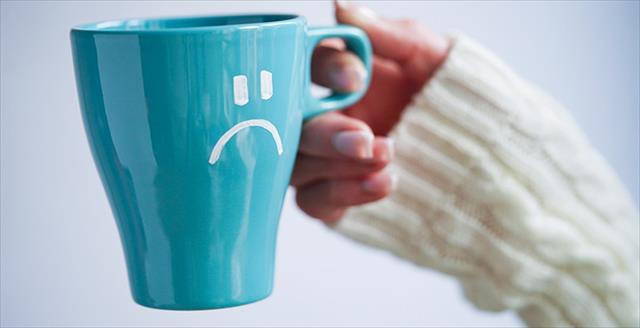 hand holding a coffee mug that has a sad emoji face on it