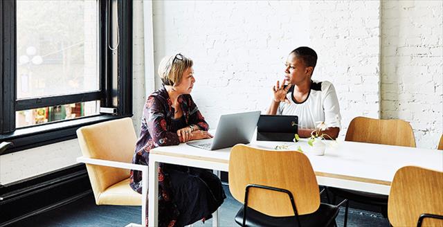 two women sitting in front of laptops having a conversation