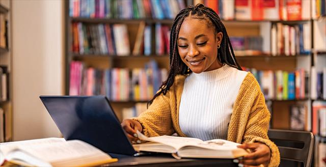 young woman reading a book at a table in a library