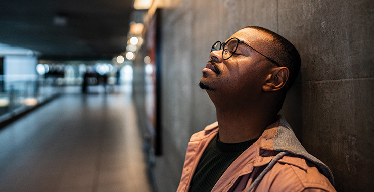 man standing with eyes closed and head back against a wall