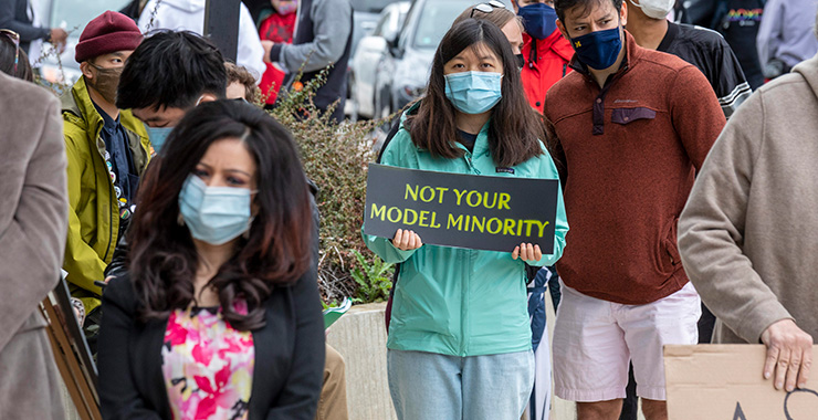 Woman in a crowd of people wearing a medical mask holding a sign