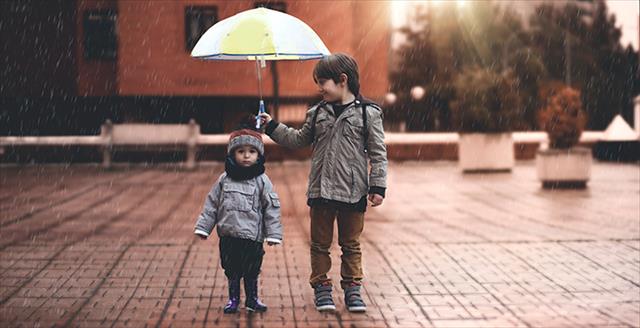 boy holding umbrella over younger boy