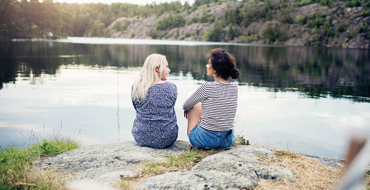 two women sitting by a lake