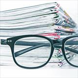 black eyeglasses in front of stack of journals