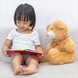 young girl reading book to teddy bear