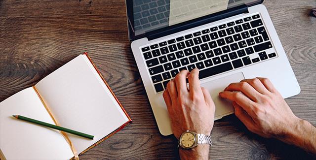 man typing on laptop keyboard with notebook and pencil next to him