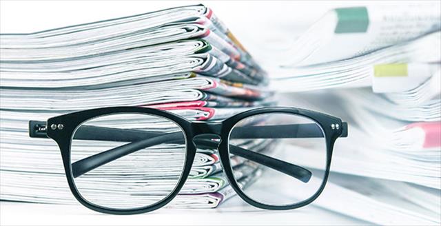 black eyeglasses in front of stack of journals