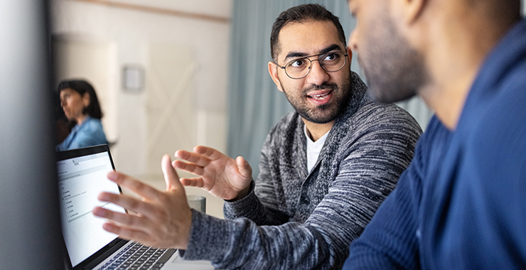 Two young professional men using a laptop engaging in conversation.
