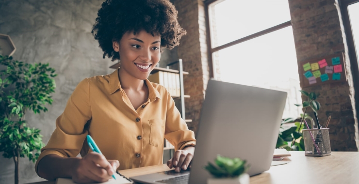 Woman taking notes and smiling in front of laptop