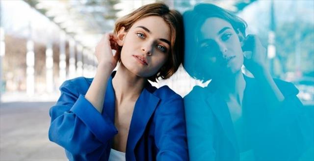 Woman leaning against a wall in a blue shirt.