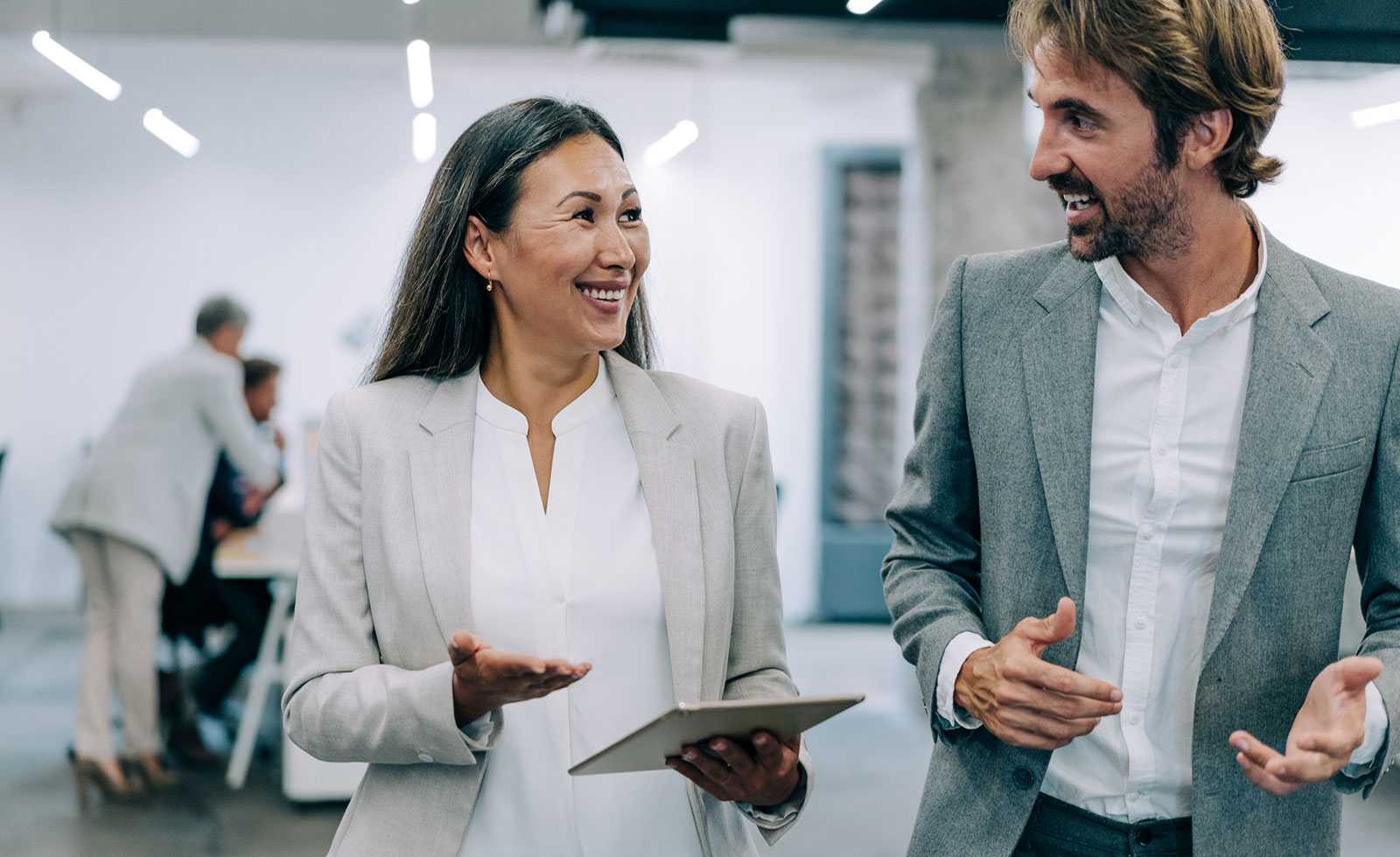 Older Asian woman speaks to younger male colleague in the office.