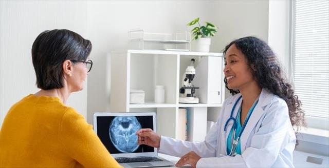 Woman with physician discussing health, seated by a desk with a brain scan on a computer screen.