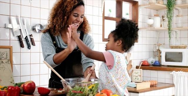 Mother and daughter in a kitchen with fresh vegetables, giving a high five.