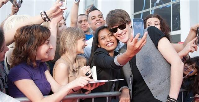 Happy crowd of fans, and a woman taking a selfie with a smiling famous man.